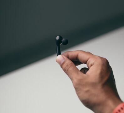 Close-up of a hand holding a modern wireless earbud, emphasizing technology and style.