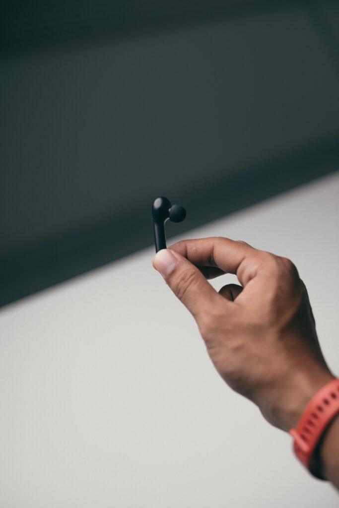 Close-up of a hand holding a modern wireless earbud, emphasizing technology and style.