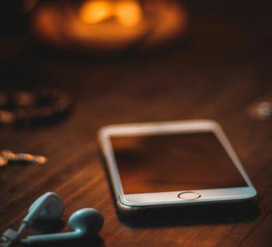 Mobile phone with earphones on a wooden table in warm ambient light, creating a cozy atmosphere.