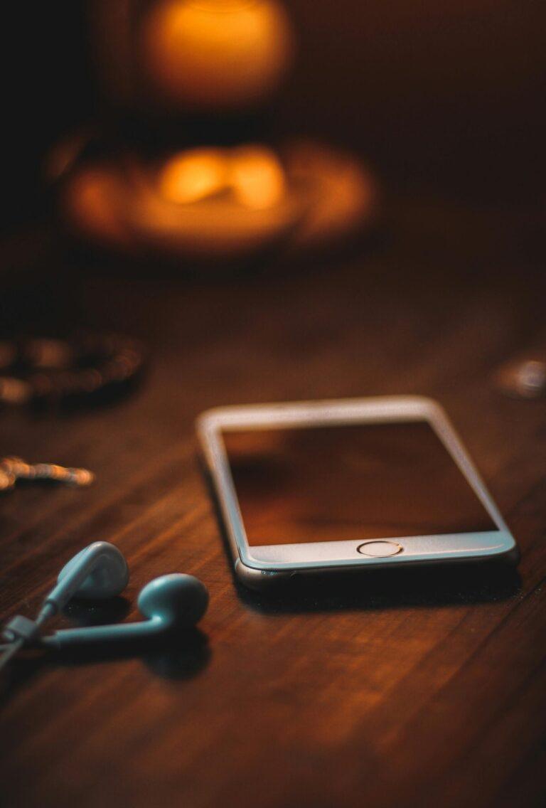 Mobile phone with earphones on a wooden table in warm ambient light, creating a cozy atmosphere.