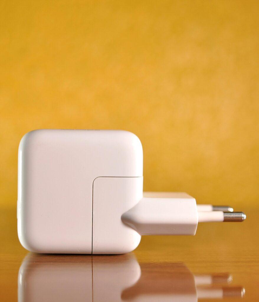 White power adapter against a warm, yellow background on a reflective surface.