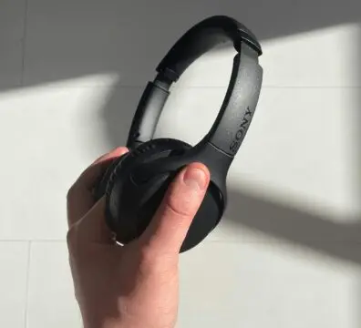 Close-up of a hand holding black wireless headphones with sunlight casting shadows.