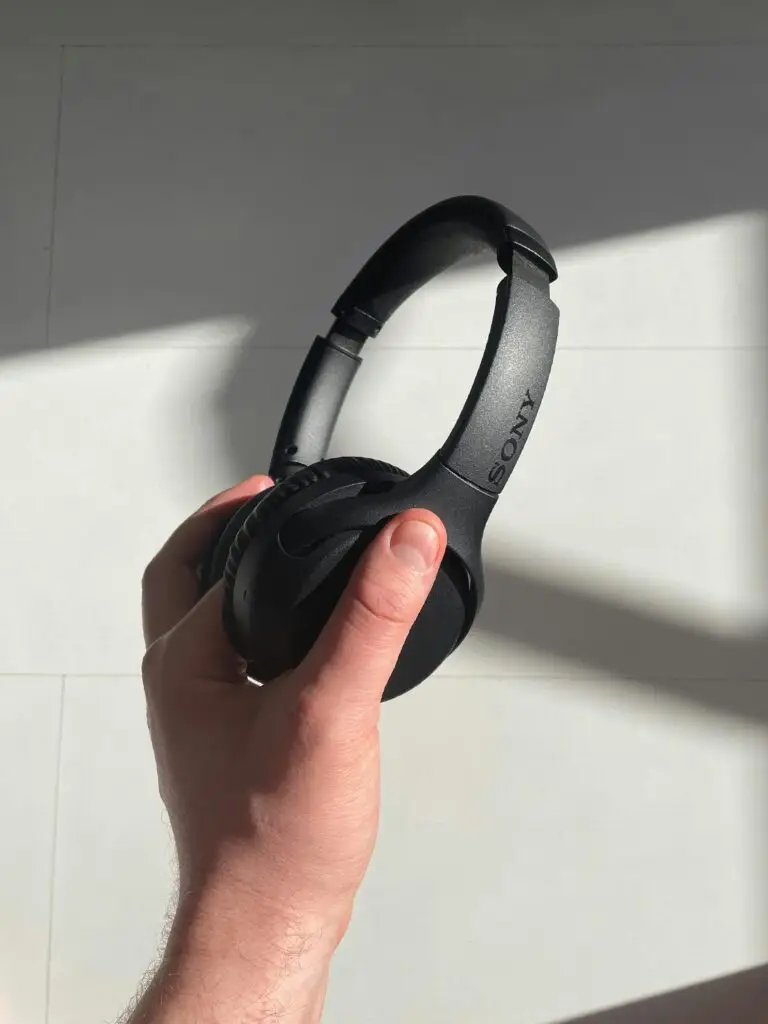 Close-up of a hand holding black wireless headphones with sunlight casting shadows.