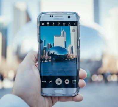 Hand holding smartphone capturing Cloud Gate reflection in Chicago skyline.