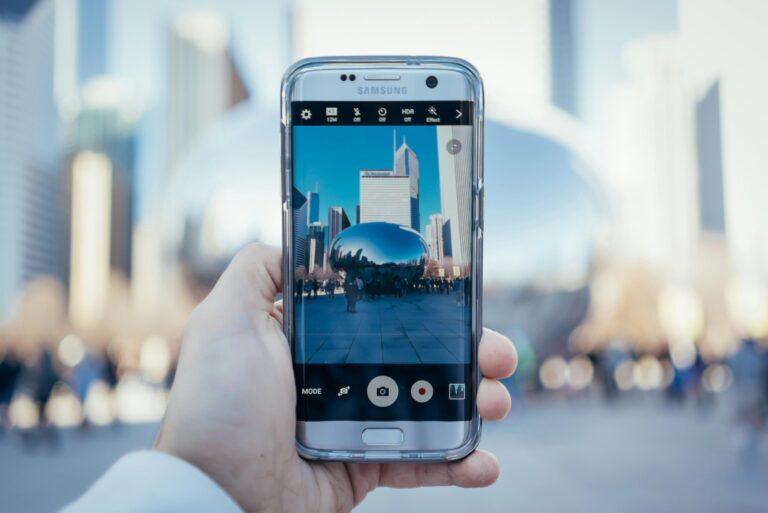 Hand holding smartphone capturing Cloud Gate reflection in Chicago skyline.