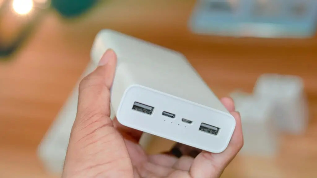 Hand holding a powerbank showcasing its USB ports on a wooden background.