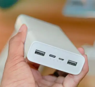 Hand holding a powerbank showcasing its USB ports on a wooden background.