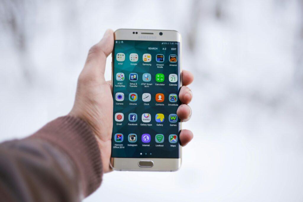 Close-up of a hand holding a Samsung smartphone displaying various app icons, emphasizing technology and connectivity.