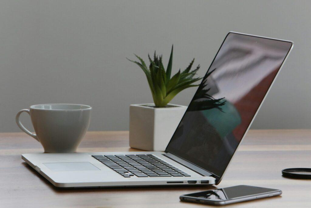 Minimalist home office desk with laptop, smartphone, and plant for a modern work environment.