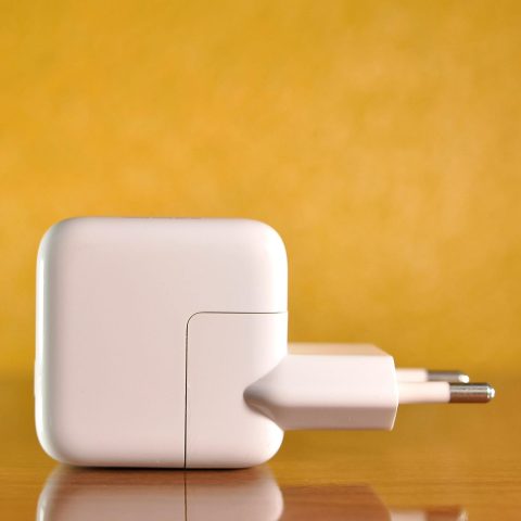 White power adapter against a warm, yellow background on a reflective surface.